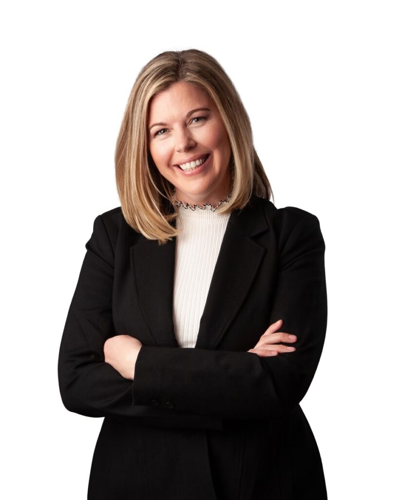 Brigette Keener, OD headshot. standing in black suit with arms crossed smiling against a white background